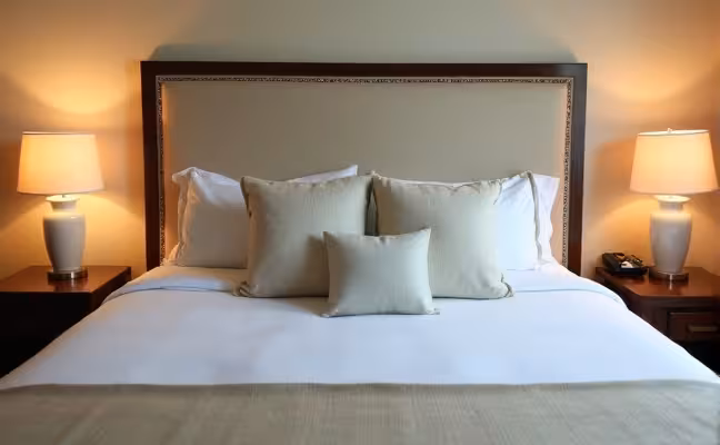 A well-made bed in a cozy guest room, adorned with high-quality bedding in soft, soothing colors. The bed should have a medium-firm mattress and a variety of different pillows, demonstrating the comfort and choice available for guests
