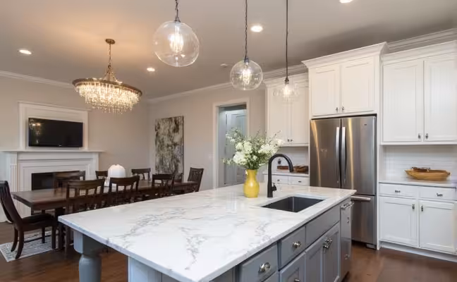 A contemporary kitchen scene with upgraded lighting fixtures, including stylish pendant lights hanging over a marble kitchen island and a chic chandelier in the adjoining living area
