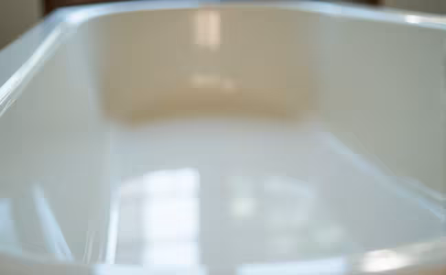 A detailed close-up of a beautifully refinished bathtub. The tub, formerly worn and old, now gleams as if brand new, reflecting the light in its shiny, polished surface